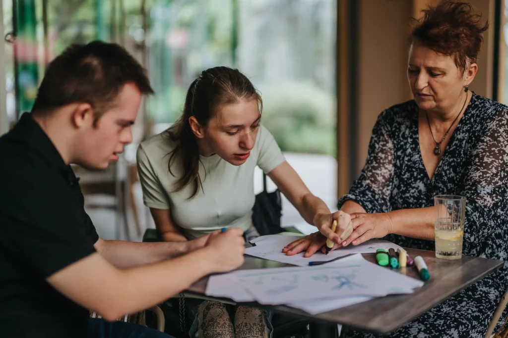 Two disabled friends drawing with support worker