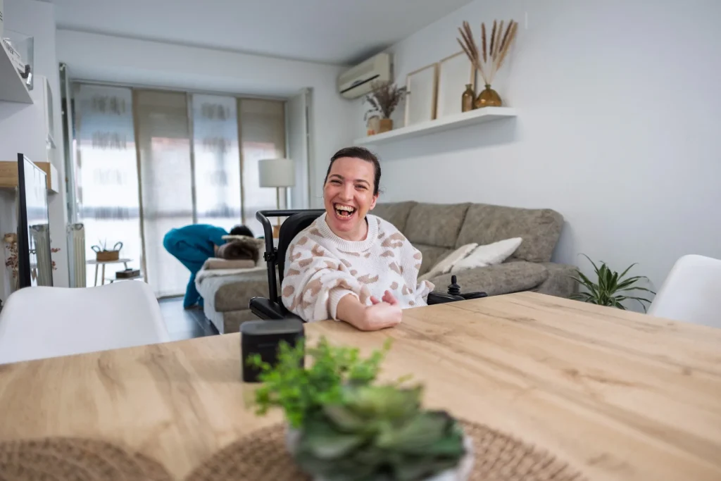 Disabled woman in wheelchair sitting at kitchen table smiling